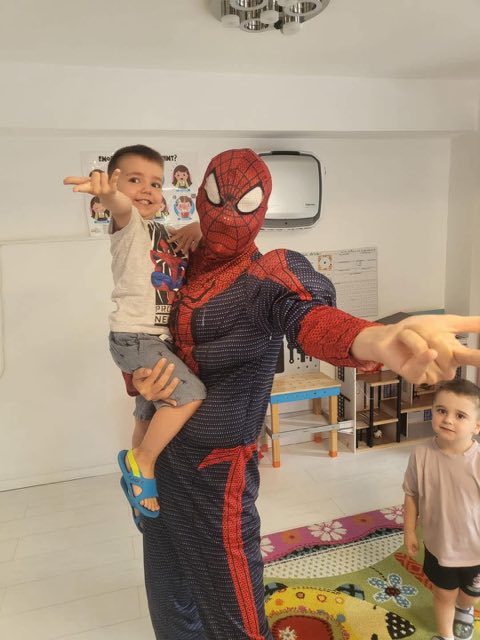 Animator în costum de supererou ținând în brațe un copil zâmbitor
