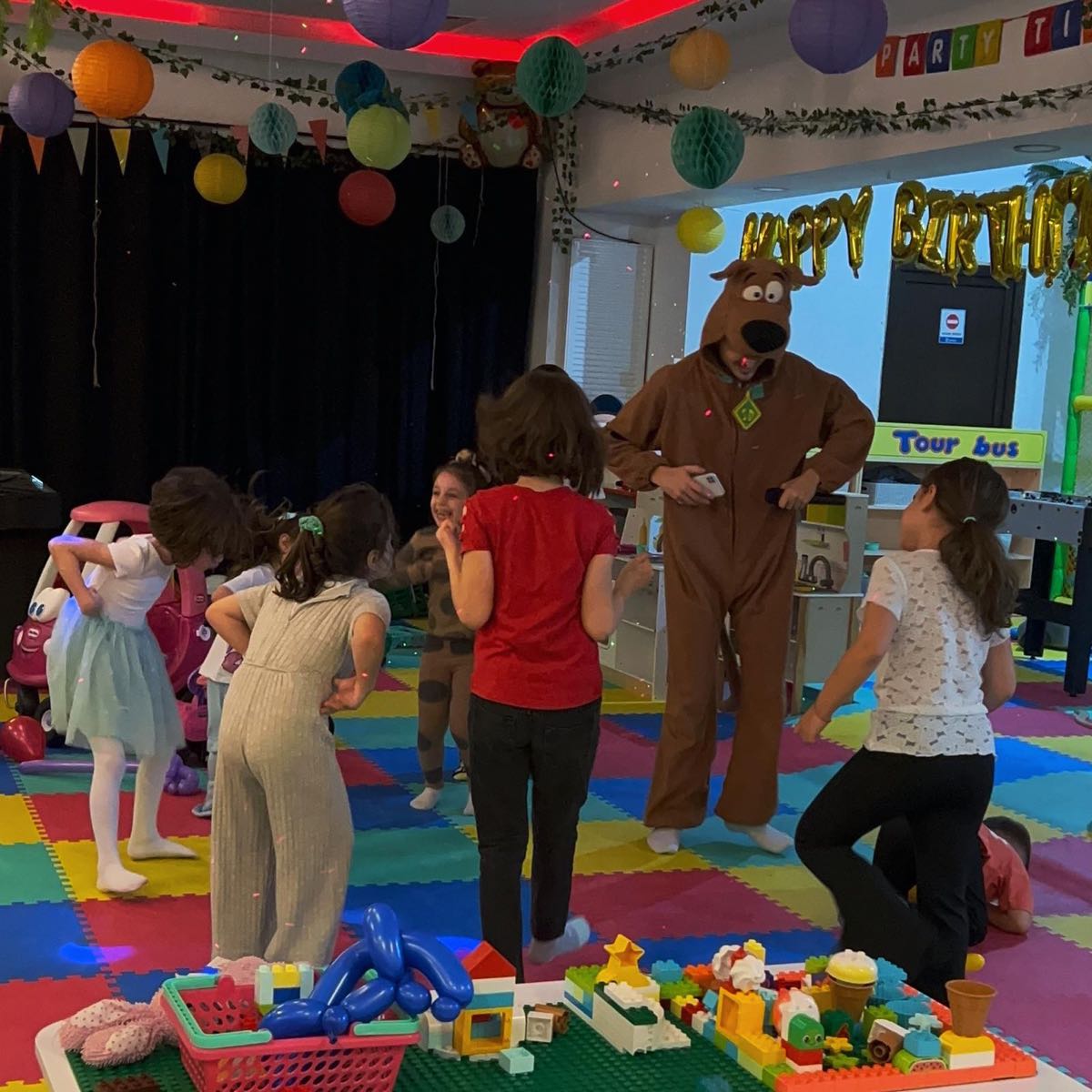 Animator în costum de cățel dansând cu copiii într-un loc de joacă decorat pentru aniversare