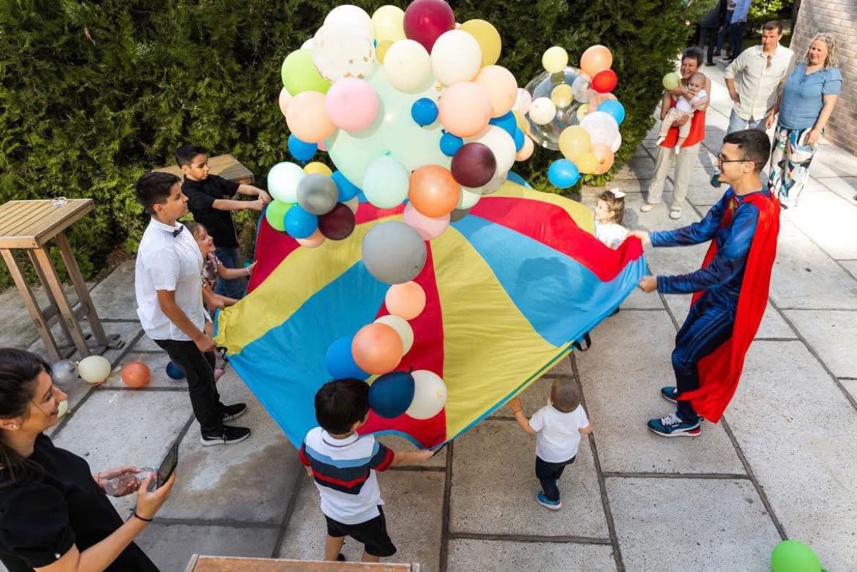 Joc cu parașuta și zeci de baloane colorate, în curte, la o petrecere de copii