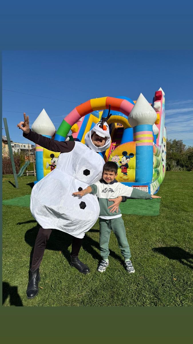 Animator și copil în fața unui castel gonflabil, la o petrecere în aer liber